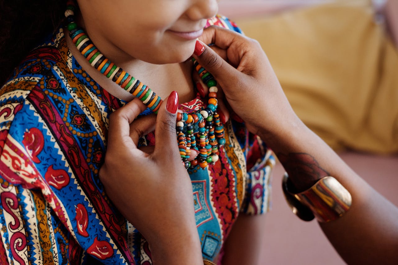 Young girl wearing a vibrant, colorful beaded necklace and traditional attire indoors.