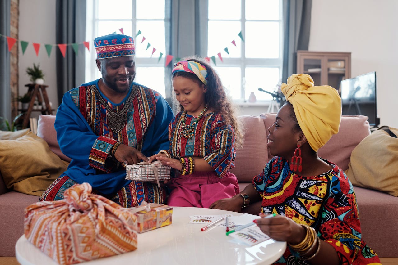 A family in traditional clothing wrapping presents and celebrating Kwanzaa indoors.